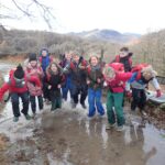 group of pupils standing and jumping in a large puddle of water and wearing waterproof clothing