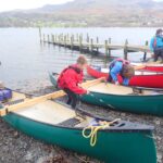 pupils dressed in waterproffs preparing their canoes by the side of the water