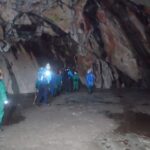 pupils in the distance entering a cave and wearing safety gear and waterproofs